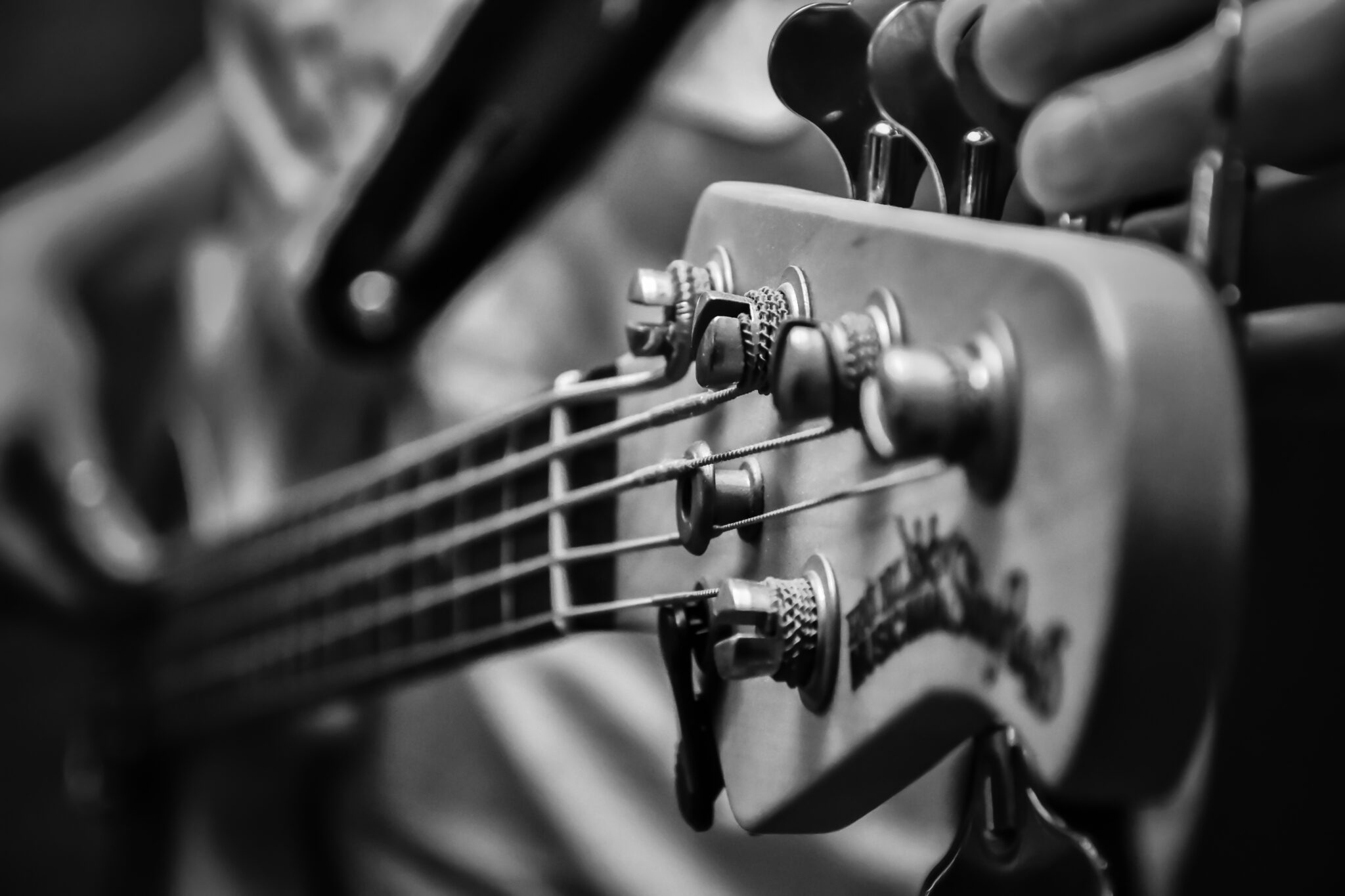 close up black and white photo of the neck of an electric bass being tuned