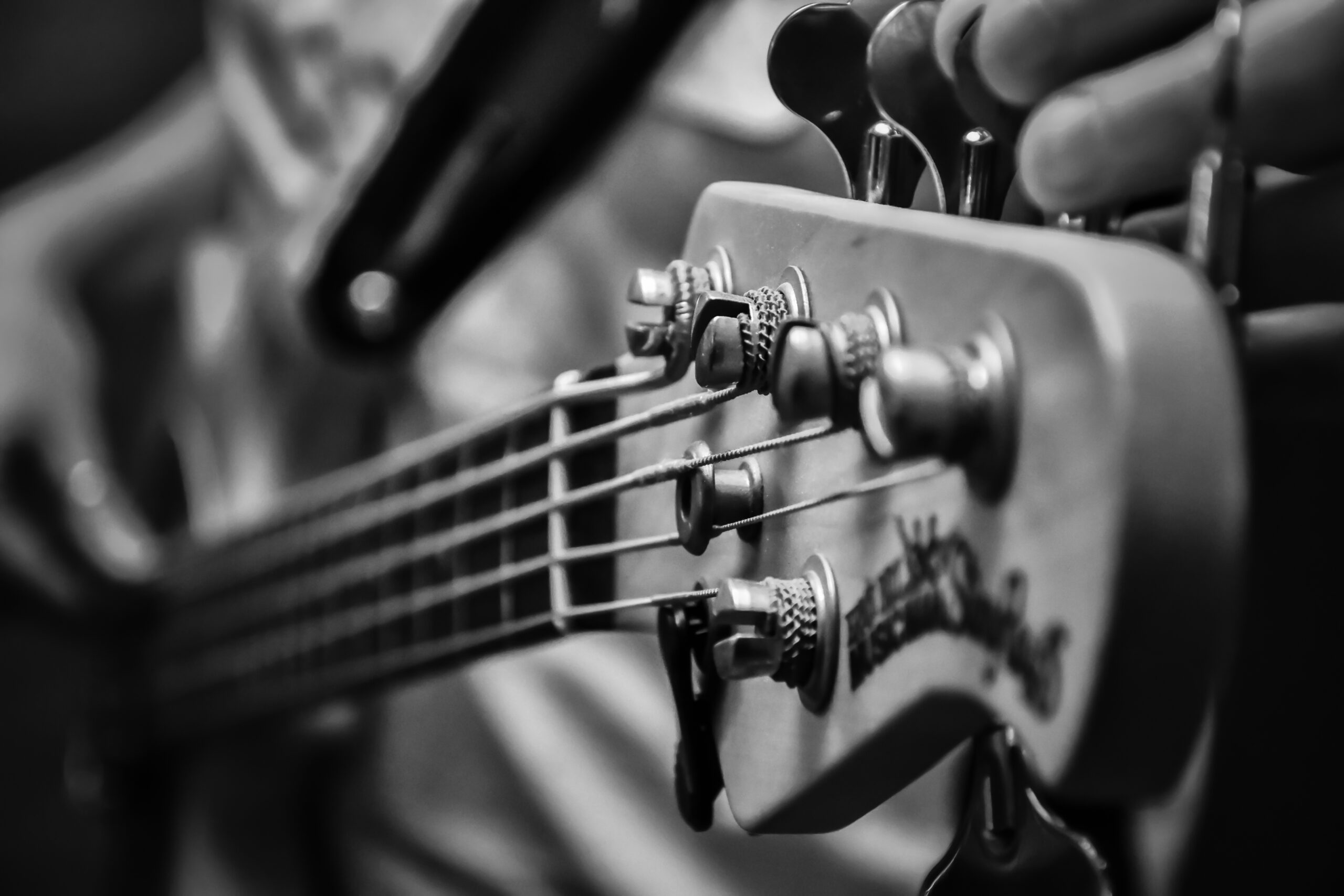 close up black and white photo of the neck of an electric bass being tuned