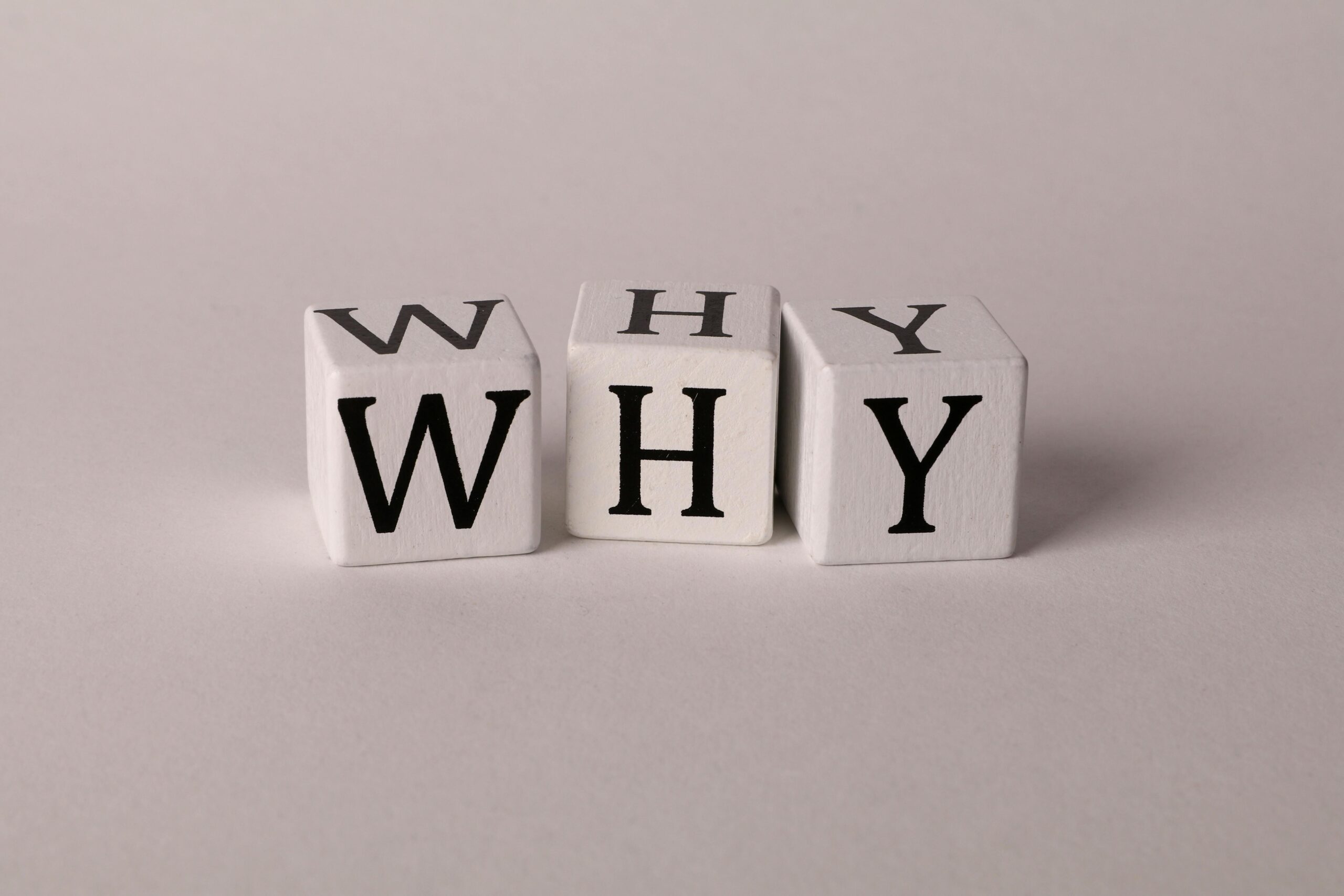 Three wooden cubes with letters printed on them spell the word "why"